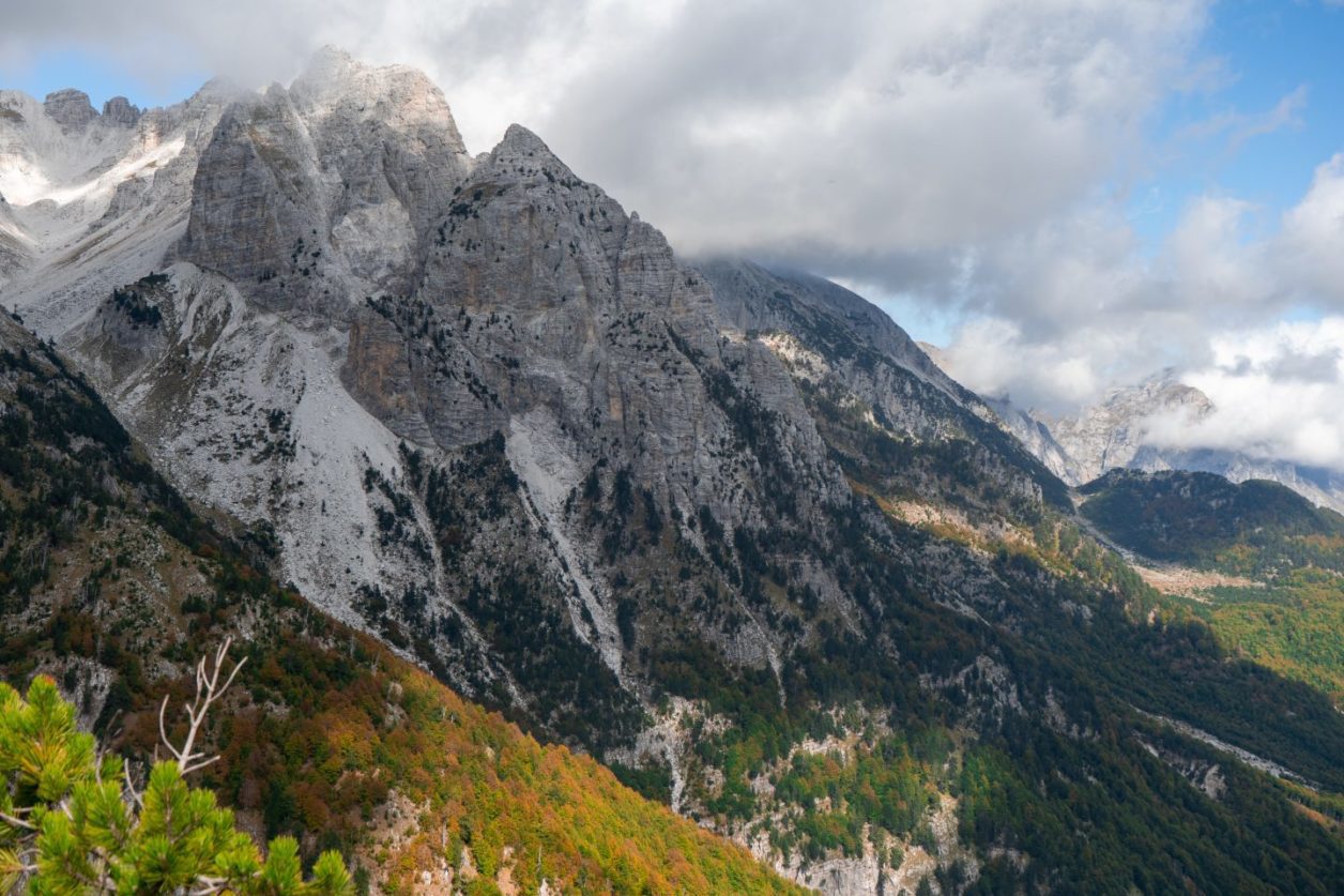 Qué hacer en Theth Albania, vista de la majestuosa cordillera con picos rocosos cubiertos de nieve que conducen al valle cubierto de hierba bajo nubes grises