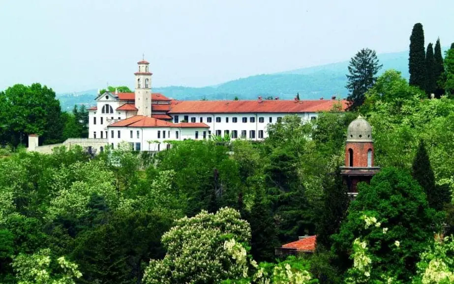 Las mejores actividades en Nova Gorica Eslovenia, monasterio blanco con techo naranja rodeado de árboles con montañas en la distancia