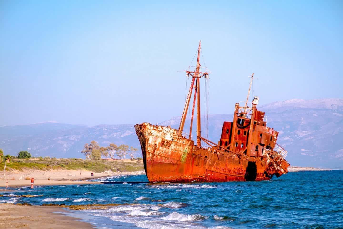 Disfruta de estos mejores lugares para visitar en Grecia para parejas, botes oxidados y en ruinas sentados junto a la costa arenosa con montañas al fondo