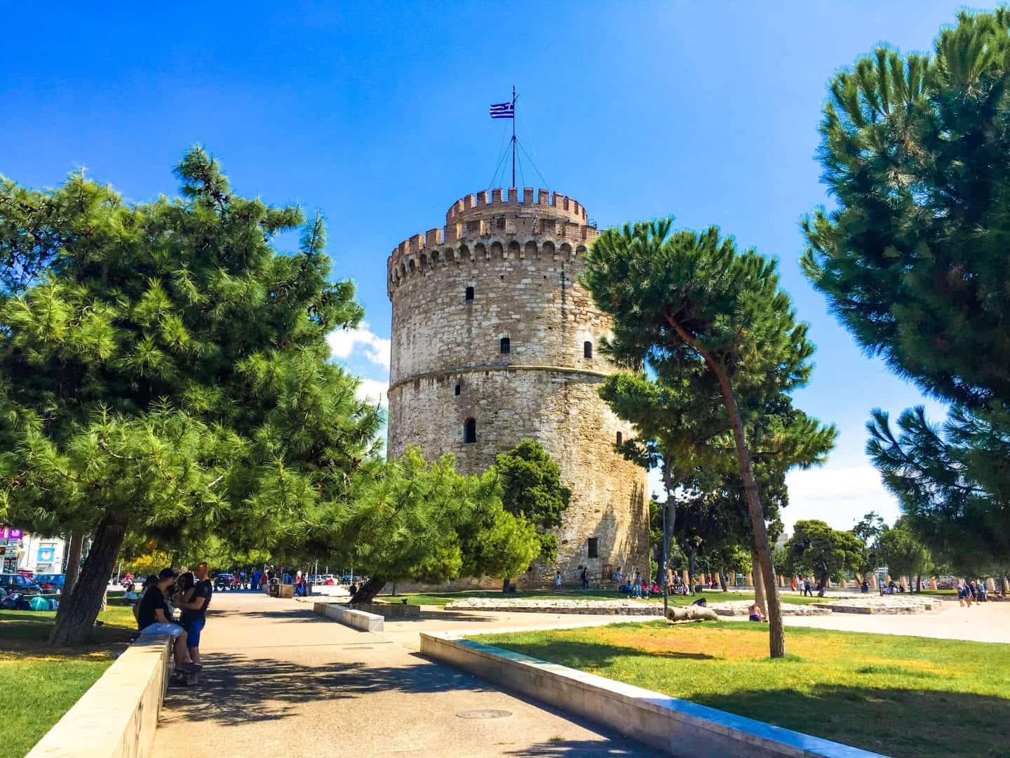 Encuentre todas las mejores atracciones en Grecia, alta torre circular de piedra en un parque con áreas de césped y árboles con gente sentada y caminando
