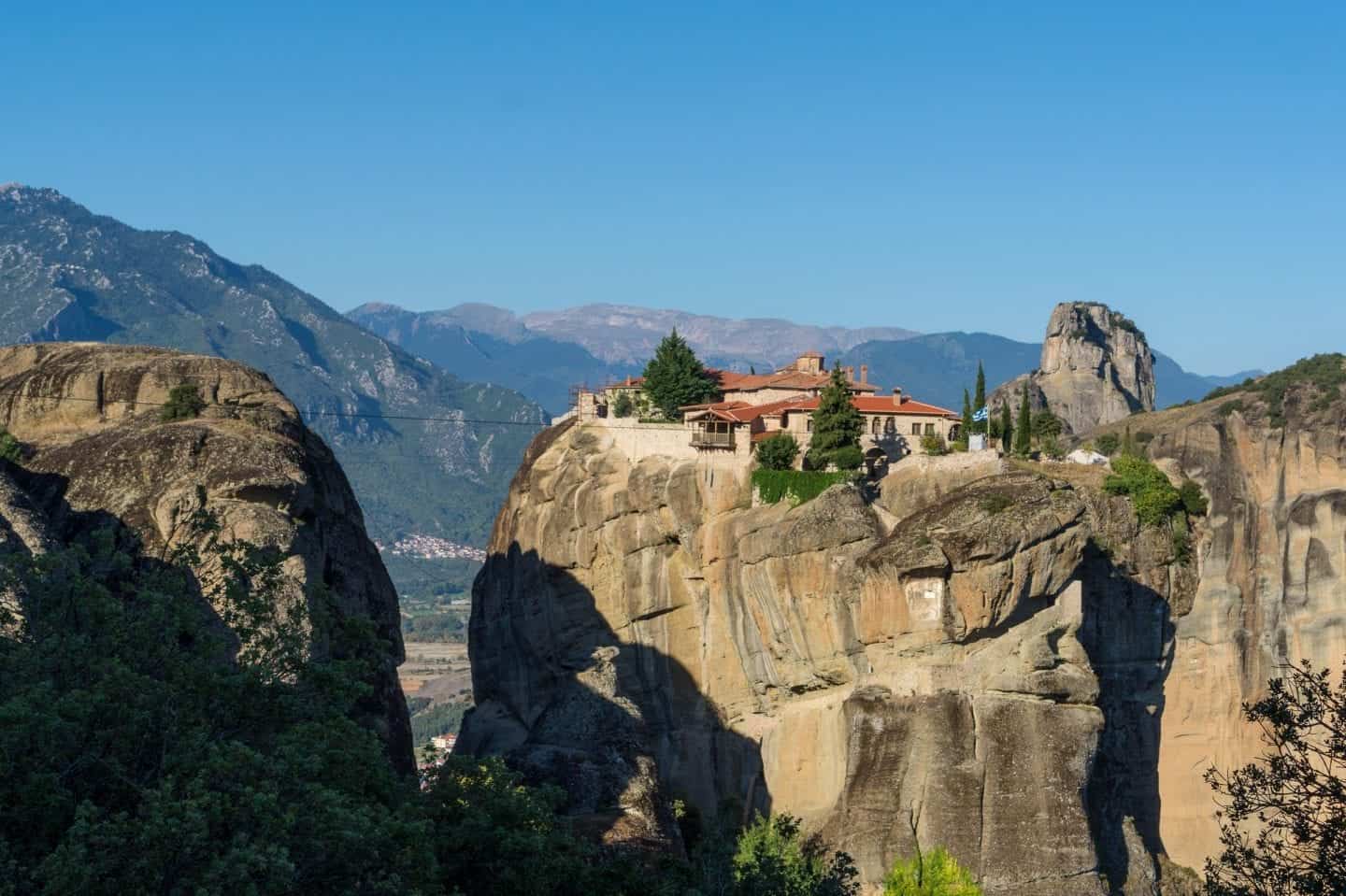 ¿Podrían ser estos los lugares más bellos de Grecia, altas montañas rocosas con un edificio antiguo construido en el borde del acantilado con grandes montañas a lo lejos bajo un cielo azul claro