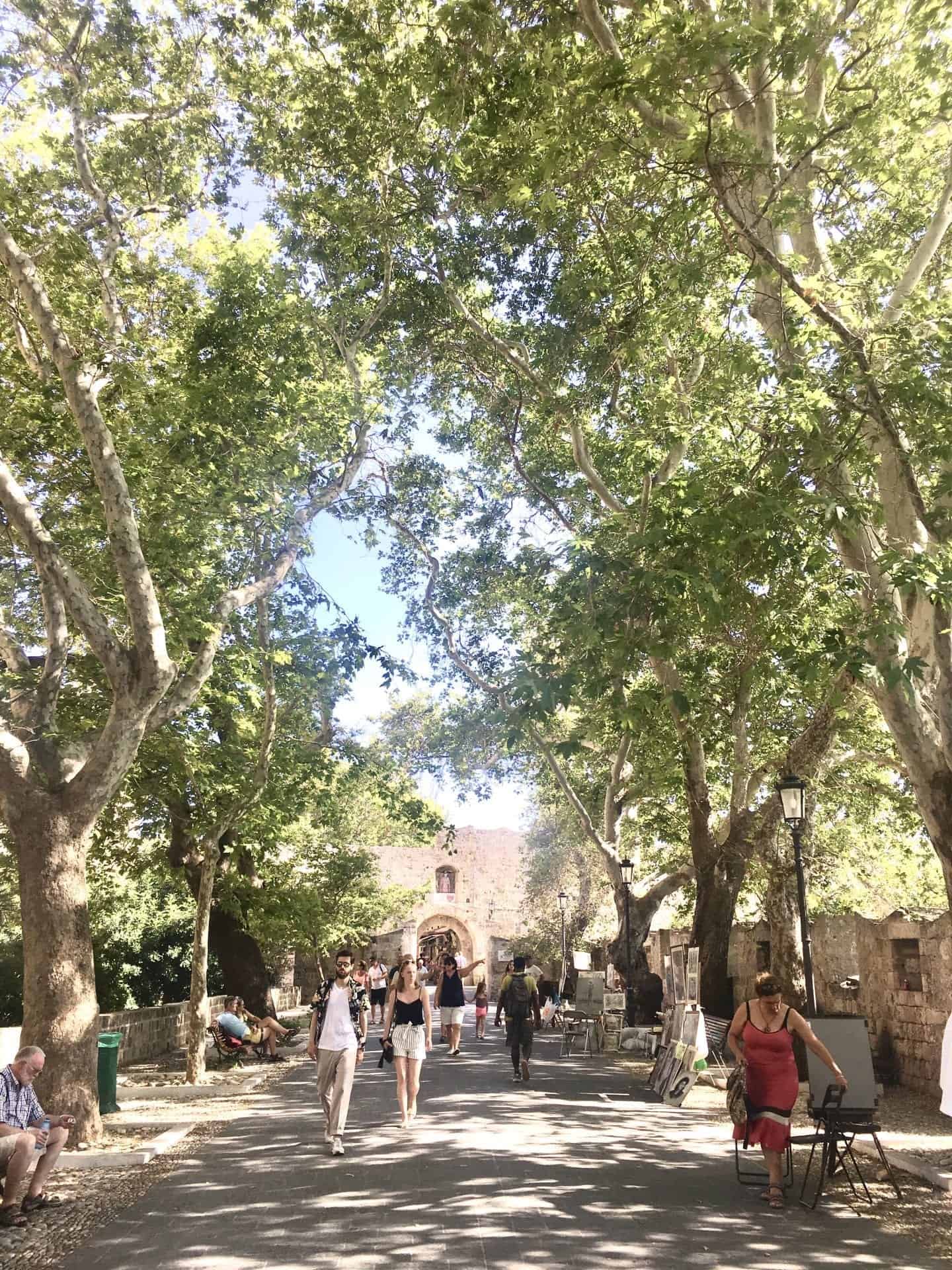 Disfrute de estos lugares famosos en Grecia, la gente camina por la calle bordeada de árboles mientras los lugareños venden artesanías al lado del la carretera