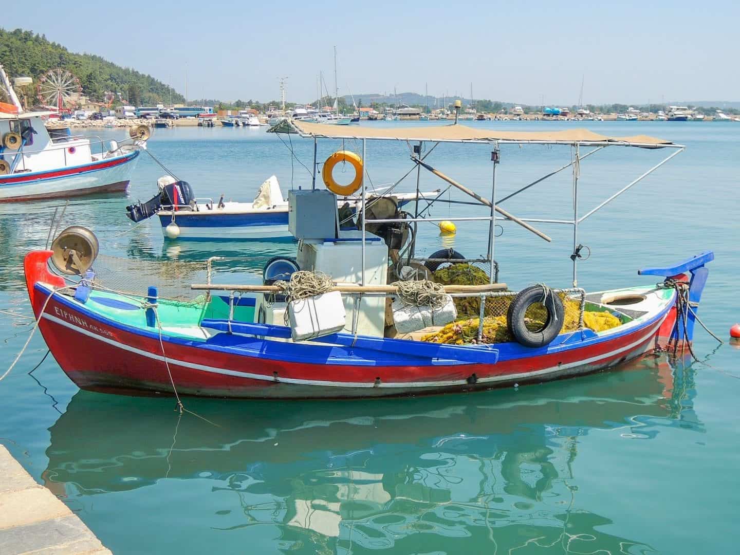 Descubre el mejor lugar para ir en Grecia este otoño, colorido barco amarrado en el puerto con aguas turquesas bajo un cielo gris