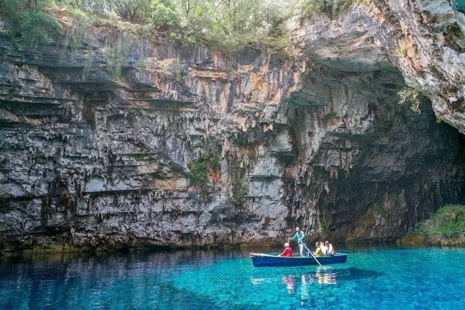 Únase a otros en estos lugares famosos de Grecia, gente en un bote de remos flotando en aguas cristalinas en un lago rodeado de altos acantilados rocosos