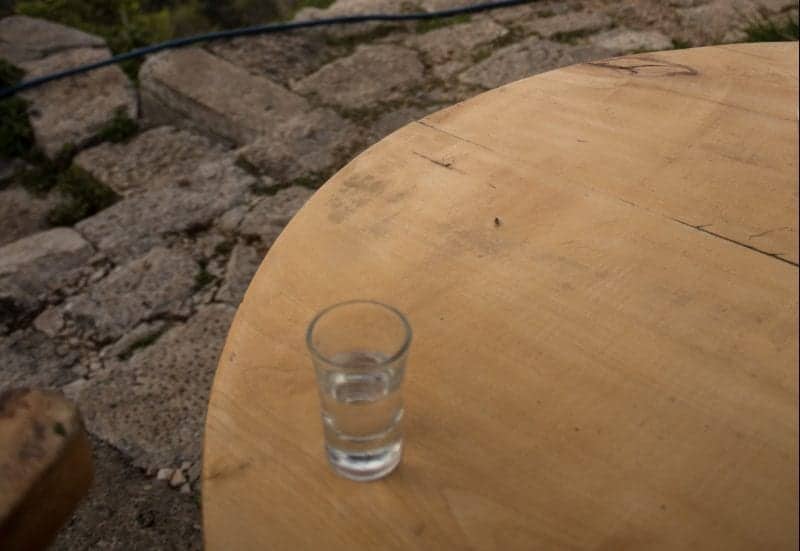 Consejos para sus vacaciones en Albania, vaso de raki en una mesa de madera afuera sobre adoquines de ladrillo gris