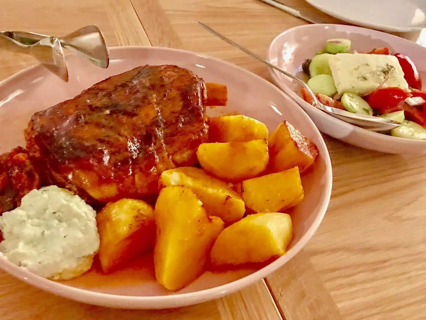 Experimente deliciosas cenas griegas tradicionales, un plato de cordero cocido a fuego lento con hueso con papas gruesas y una guarnición de queso y ensalada de tomate en platos de tazón rosa.
