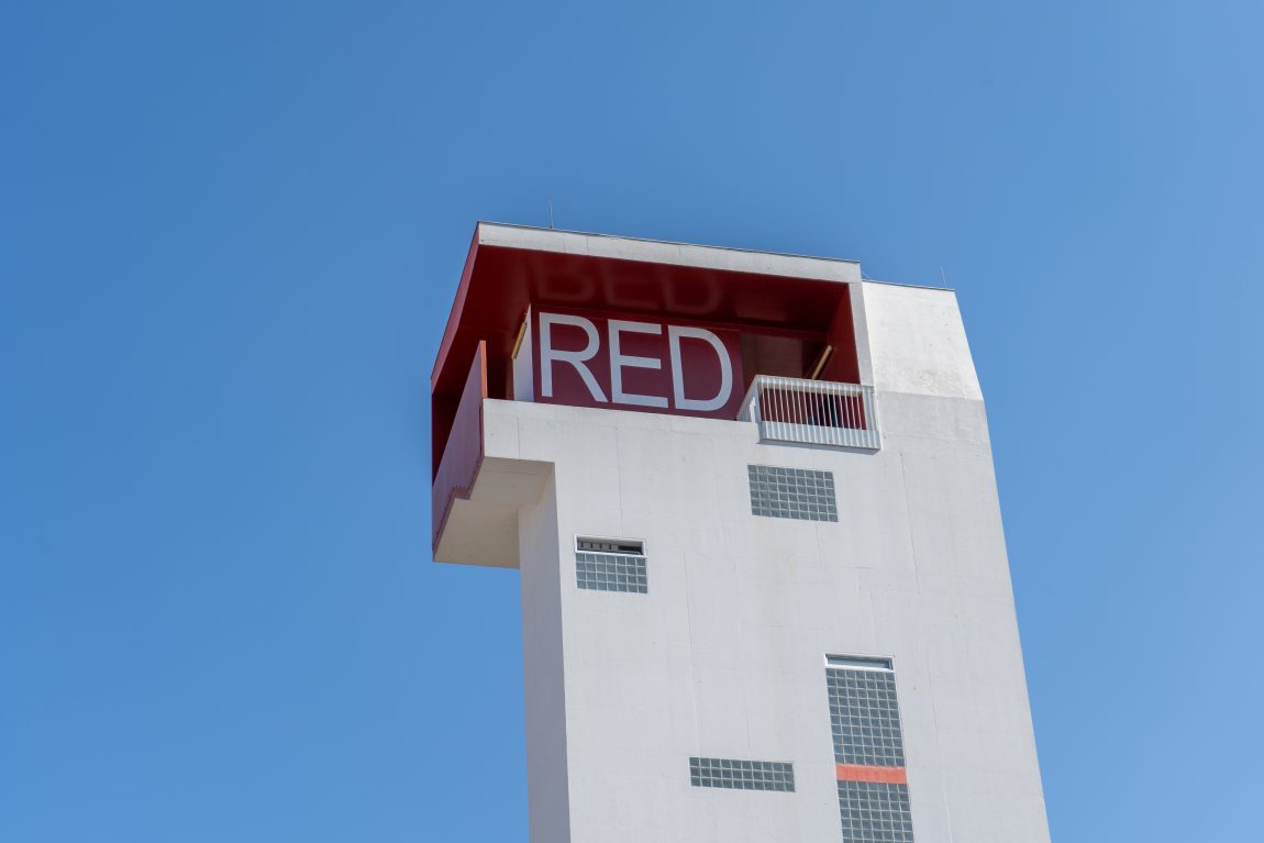 Lugares para visitar en Korca, parte superior de un edificio gris alto con un logotipo rojo brillante en el balcón bajo un cielo azul celeste