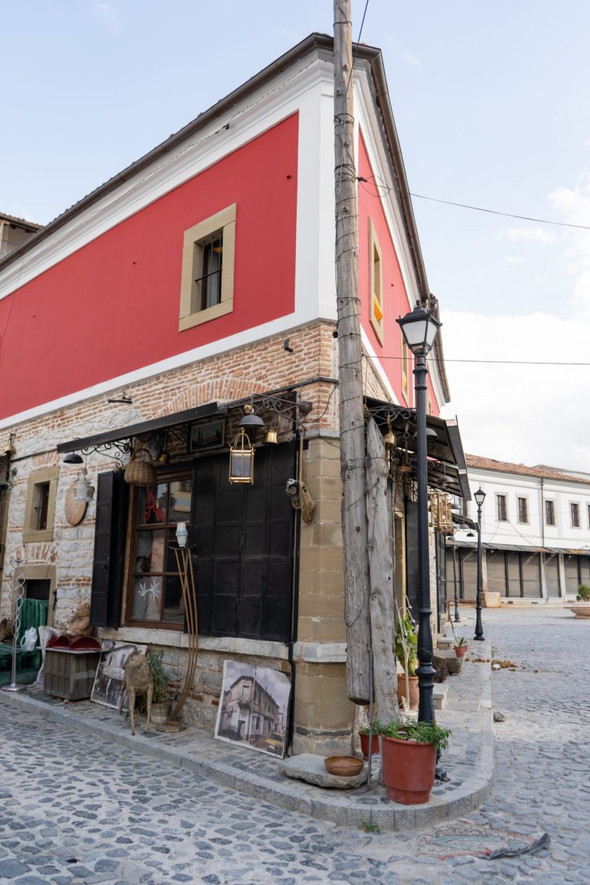 Qué visitar en Korca, esquina con edificio en forma de cuña con pintura roja y ladrillo junto a lampost y planta en maceta