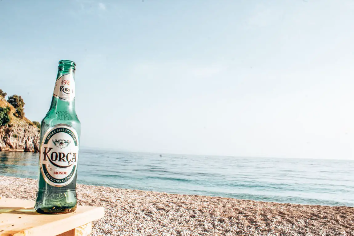 Qué hacer en Korca, botella de cerveza Korca en la mesa junto a la playa con vistas a las aguas azules