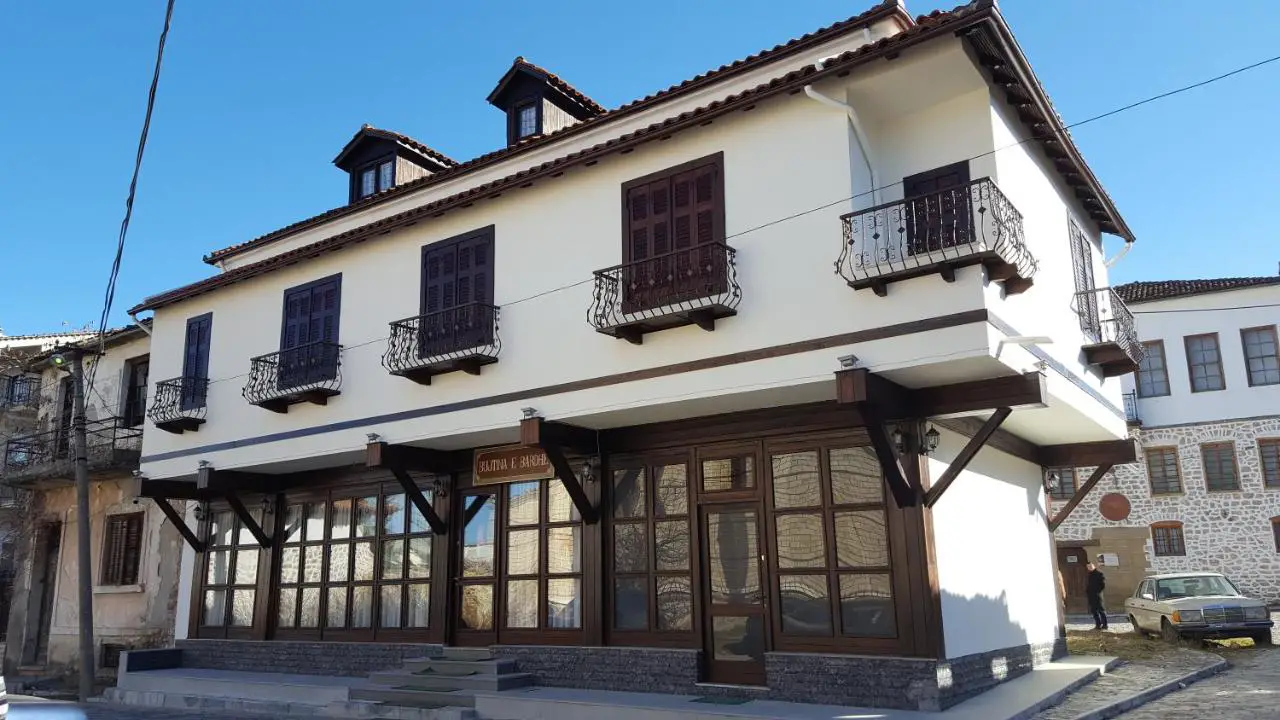 Qué hacer en la ciudad de Korca, inmaculado edificio pintado de blanco con ventanas de madera y fachada de vidrio con balcones de metal