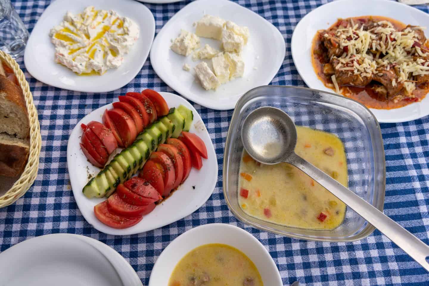 Dónde hospedarse en Theth Albania, platos de delicias albanesas que incluyen sopa, carne, queso y verduras sobre un mantel de cuadros azules