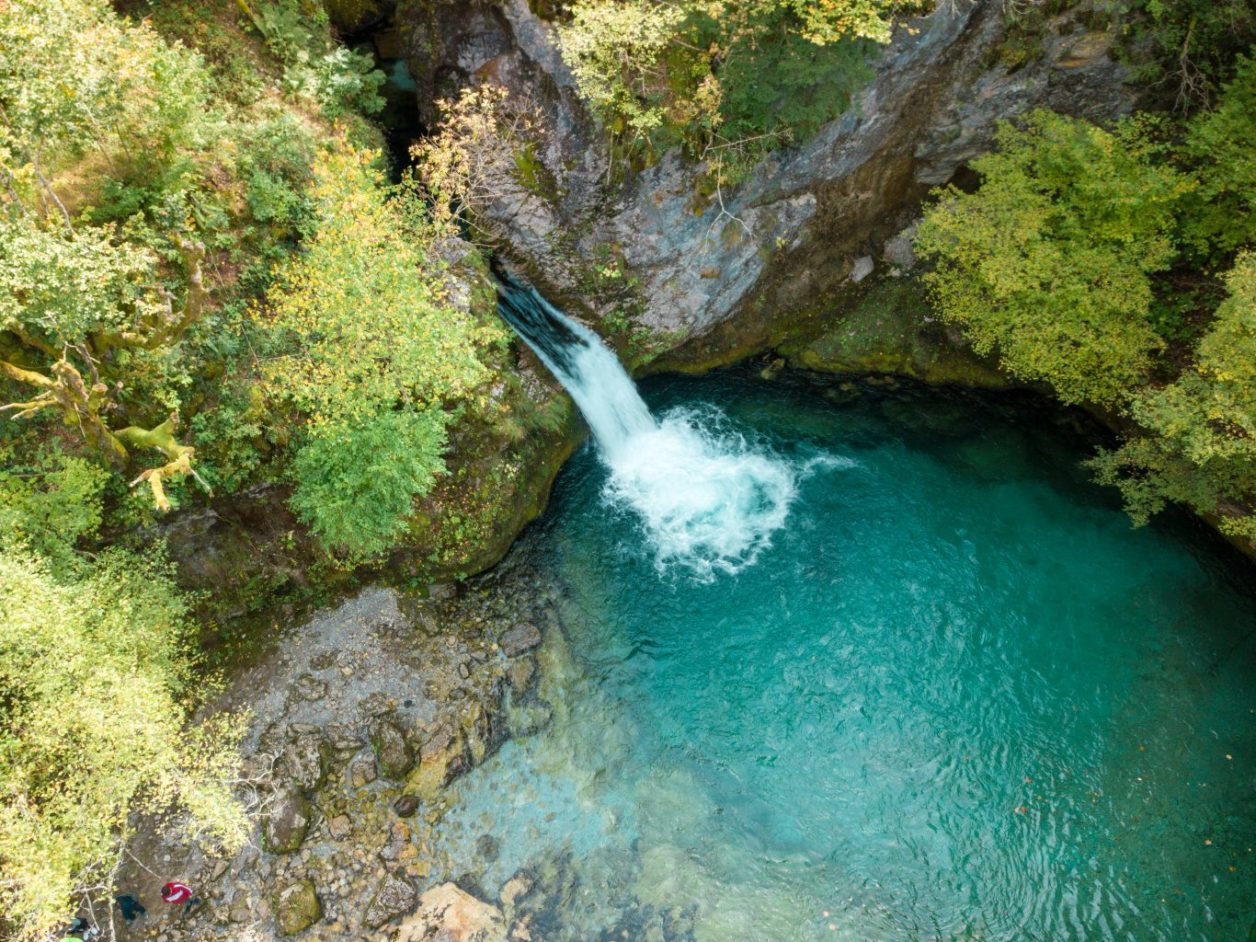 Belleza natural en el Parque Nacional Theth, cascada que cae sobre formaciones rocosas en un lago turquesa rodeado de árboles verdes