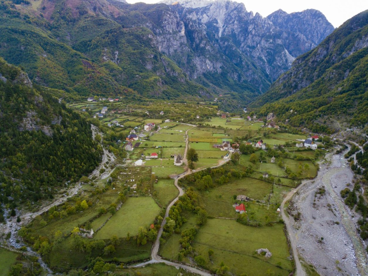 Cómo llegar a Theth Albania, vista del pueblo de Theth con edificios antiguos salpicados de mosaicos de campos verdes rodeados de altas montañas por todos lados
