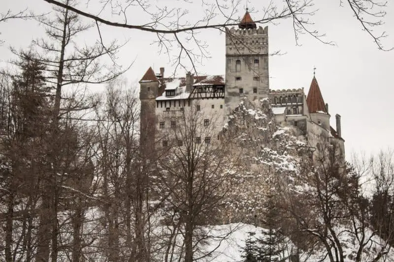 Castillos góticos en Europa que hay que verlos para creerlos, altos e imponentes castillos de piedra gris con torreones de punta marrón rodeados de ramas desnudas de árboles de invierno bajo una capa de nieve blanca