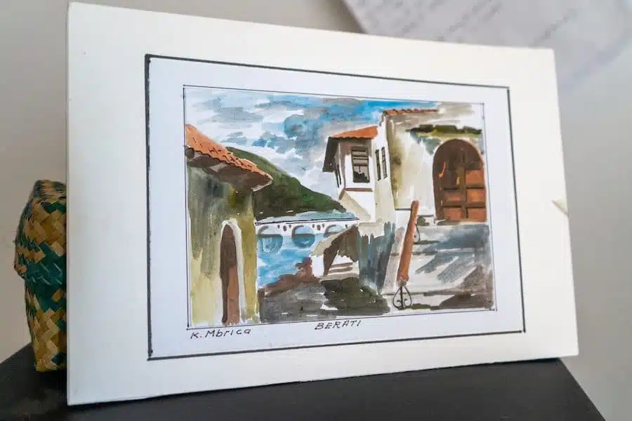 Los dibujos y el arte son excelentes recuerdos albaneses, pintura de K. Mbrica que representa una escena de casas, un puente y un río.