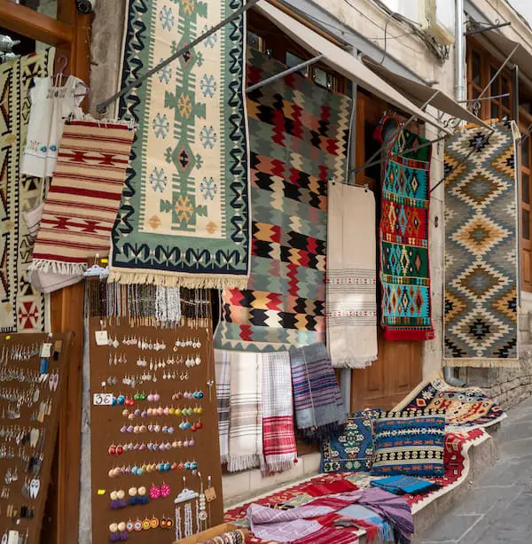 Los mejores recuerdos albaneses para comprar, el exterior de una tienda de recuerdos albaneses con aretes coloridos, alfombras y cojines con patrones vibrantes