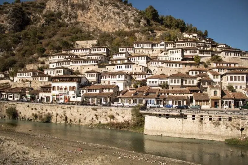 Explore las mejores ciudades para visitar en Albania, ciudad de edificios de techo de terracota dispuestos en niveles alrededor de la ladera con un muro alto junto al río circundante