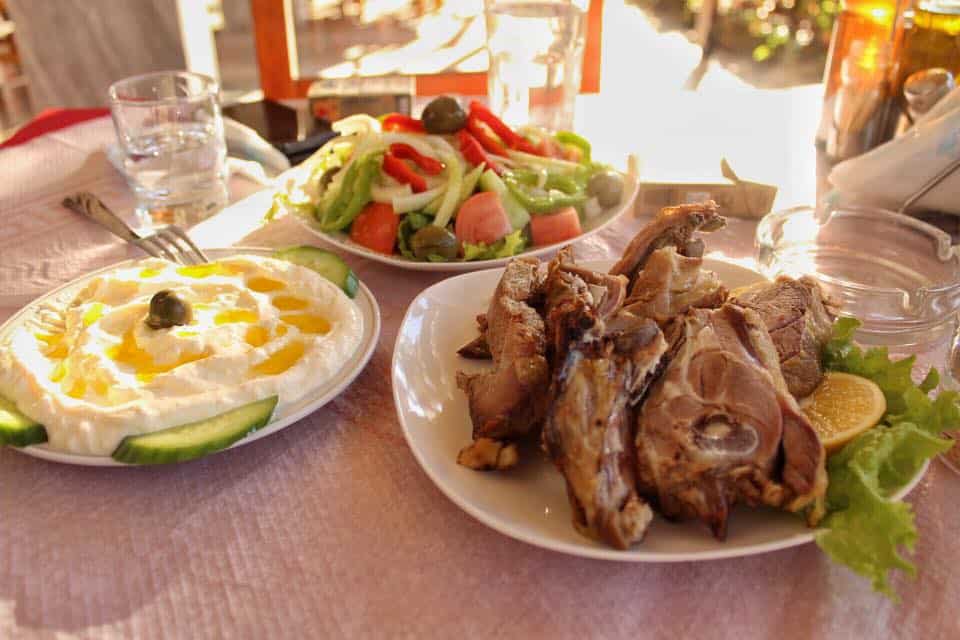 Deliciosa comida tradicional albanesa, tres platos de carne, ensalada de verduras y salsa cremosa en una mesa dentro de un restaurante