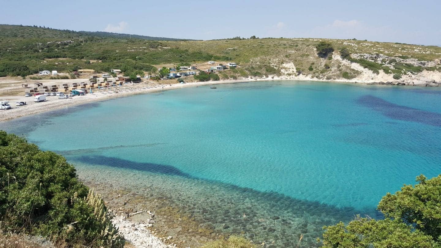 Experimente las mejores ciudades para visitar en Turquía, una gran bahía de agua azul turquesa frente a una playa de arena blanca rodeada de colinas cubiertas de hierba