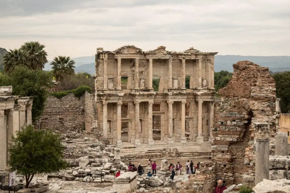 Encuentre los lugares más bellos de Turquía, un grupo de personas lijando frente a las ruinas de una gran estructura con pilares de piedra y puertas altas bajo un cielo gris