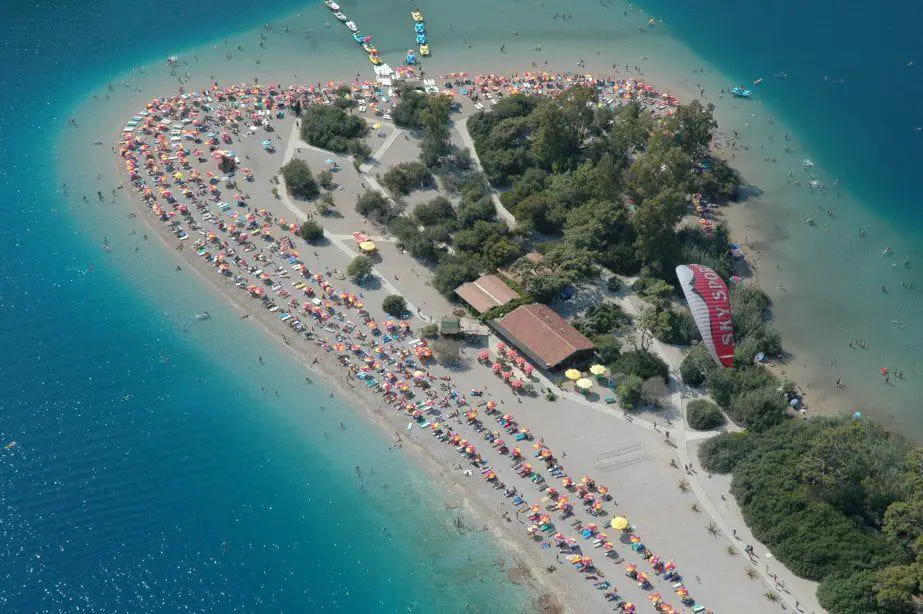 Pruebe todas las mejores cosas para hacer en Turquía, vista aérea de la península arenosa cubierta de tumbonas y sombrillas de playa con árboles y edificios rodeados de agua de mar azul claro