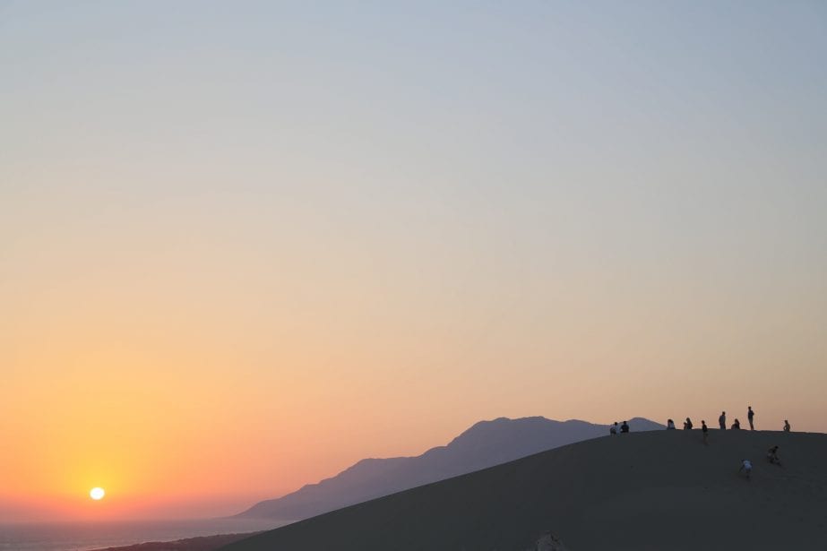 Descubre todos estos lugares de visita obligada en Turquía, siluetas de personas de pie en una duna de arena con la puesta de sol en la distancia