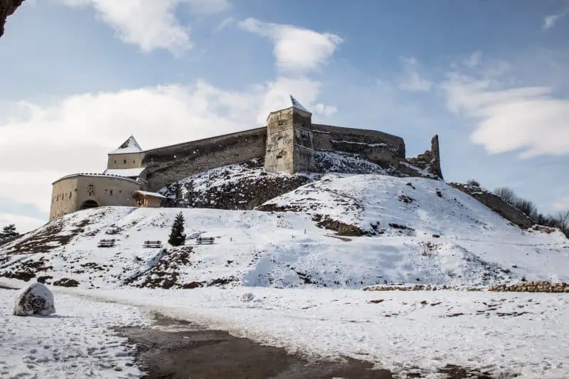 destinos europeos más baratos para visitar ahora, fortaleza de piedra en la cima de una colina cubierta de nieve en un día soleado