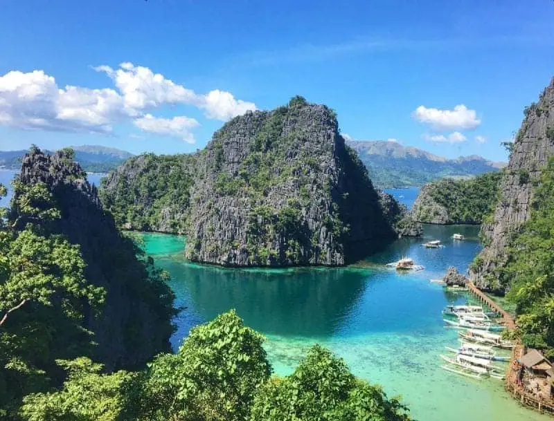 La belleza de las islas Filipinas, altas formaciones rocosas cubiertas parcialmente de follaje verde con aguas sinuosas y botes de remos de madera recogidos a un lado, así como remar río abajo con montañas en la distancia.