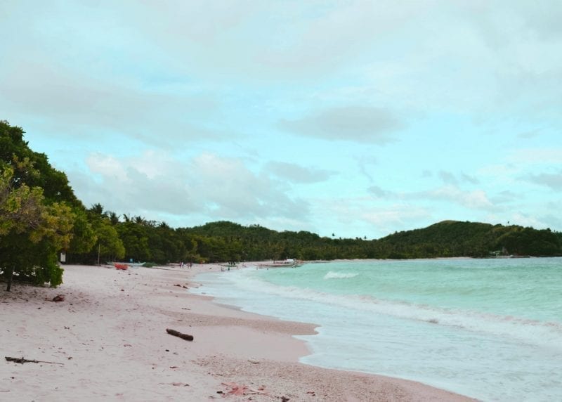 Las mejores islas de Filipinas, una larga playa de arena que se curva alrededor de árboles verdes y olas azules