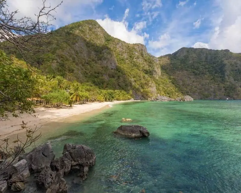 La isla más hermosa de Filipinas, rocas en aguas turquesas cerca de una playa de arena con árboles y montañas cubiertas de verde que se curvan alrededor de una cala