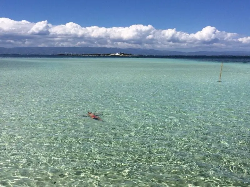 La mejor isla de Filipinas, persona flotando en agua clara bajo un cielo azul profundo con un banco de nubes blancas y esponjosas e islas a lo lejos