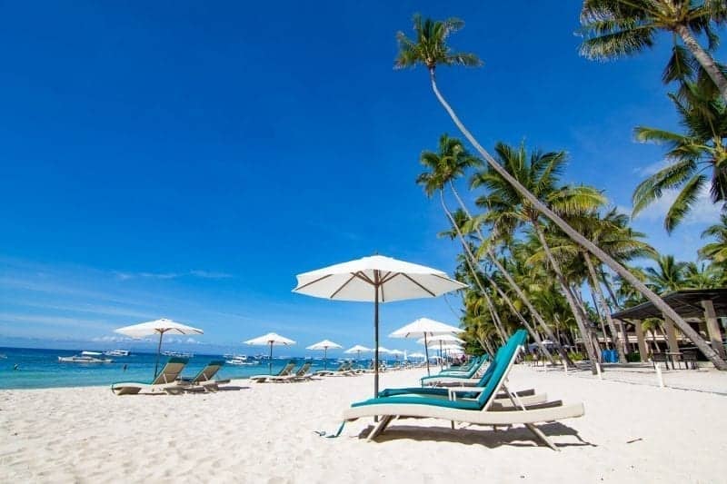 Islas subestimadas en Filipinas, sillas de playa y sombrillas junto a palmeras con vistas a la playa de arena y agua azul