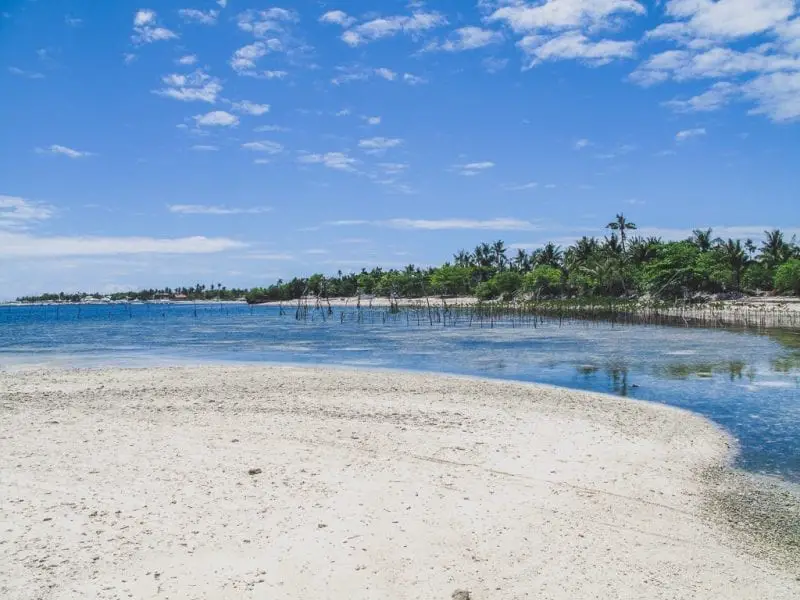 Hermosa isla en Filipinas, playa de arena con agua poco profunda y árboles verdes bajo un cielo azul con nubes