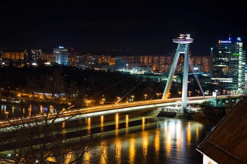 Encuentre las mejores ciudades europeas para visitar en invierno, un gran puente moderno sobre un río ancho junto a una gran área metropolitana con altos bloques de apartamentos iluminados despierto por la noche