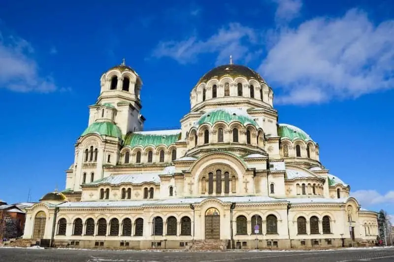 Pasee por las mejores ciudades europeas para visitar en diciembre, el gran edificio de la iglesia con amplios techos abovedados y piedra blanca tallada con muchas ventanas arqueadas bajo un cielo azul.