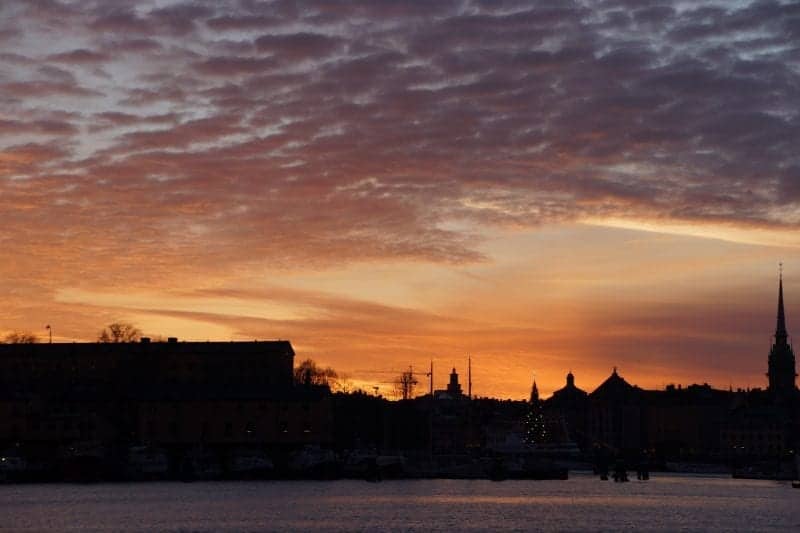 Disfrute de las mejores ciudades para visitar durante el invierno en Europa, toma atmosférica del horizonte oscuro de Estocolmo con varias torres puntiagudas y grandes edificios con techos planos bajo un cielo nublado gris y naranja al atardecer