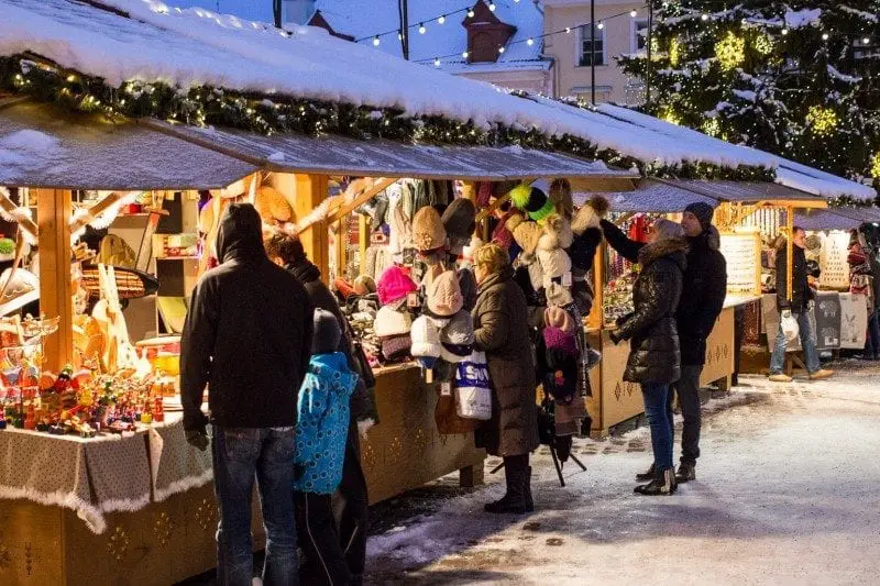 ¿Será esta la ciudad más bonita de Europa? Línea de puestos emergentes de madera en un mercado navideño cubierto por una gruesa capa de nieve blanca con personas que examinan obsequios y golosinas al atardecer