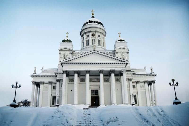 Encuentre los mejores lugares para visitar en diciembre en Europa este año, imponente iglesia blanca con tres torres abovedadas con cruces doradas sobre escalones cubiertos de nieve bajo un cielo despejado