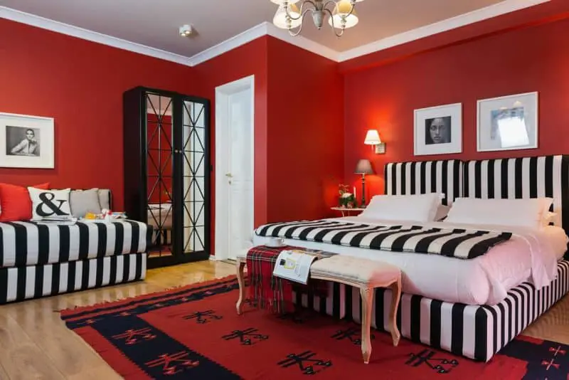 Increíble alojamiento en Tirana, gran habitación de hotel con una cama grande con sábanas a rayas blancas y negras, un sofá a juego, una gran alfombra roja y paredes rojas