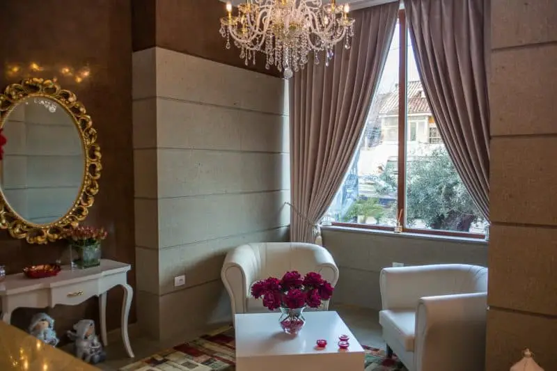 Los mejores lugares para hospedarse en Tirana, habitación con dos sillones de cuero blanco uno frente al otro en ángulo alrededor de una mesa cuadrada blanca con rosas junto a la ventana abierta en un lado y un tocador y un espejo con borde dorado en el otro lado
