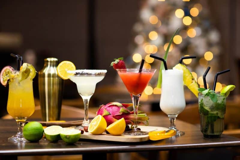 Los mejores hoteles de lujo de Tirana, mesa con cinco bebidas alcohólicas de diferentes colores, una coctelera de metal, una pitahaya entera y limones y limas en rodajas