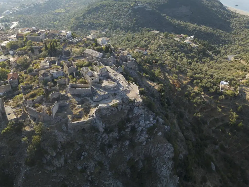 Explore los castillos de Albania, toma cenital del castillo de Himare con un gran afloramiento rocoso y muchas áreas verdes de árboles que conducen a un valle y grandes colinas más allá