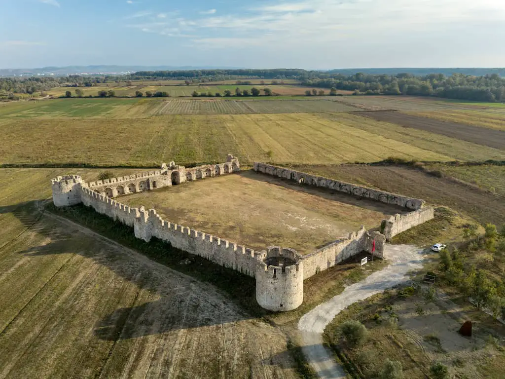 Visita tu castillo favorito en Albania, toma aérea de la fortaleza de Bashtovë con grandes muros de piedra fortificados rodeados de exuberantes campos verdes que se pierden en la distancia