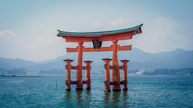 Descubre datos japoneses al azar, estructura de madera roja rodeada de agua con montañas al fondo
