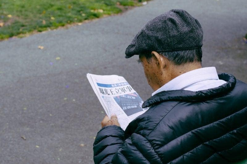 Cosas únicas sobre Japón, anciano con sombrero gris leyendo un periódico japonés en un parque