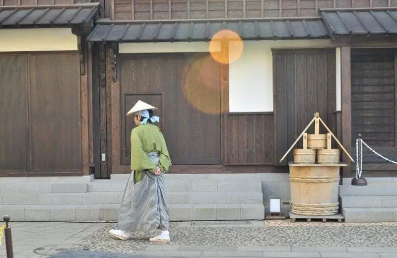 Cosas únicas sobre Japón, mujer cruzando el patio con cubos de madera apilados frente a casas con fachada de madera