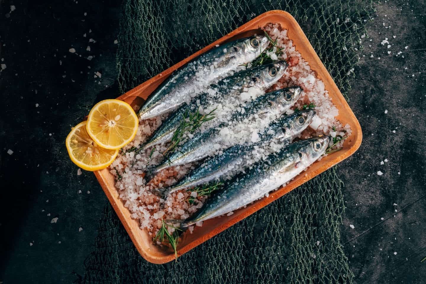 Comida tradicional albanesa para que pruebe, imagen superior de cinco pequeños pescados enteros salados en una prueba con rodajas de limón