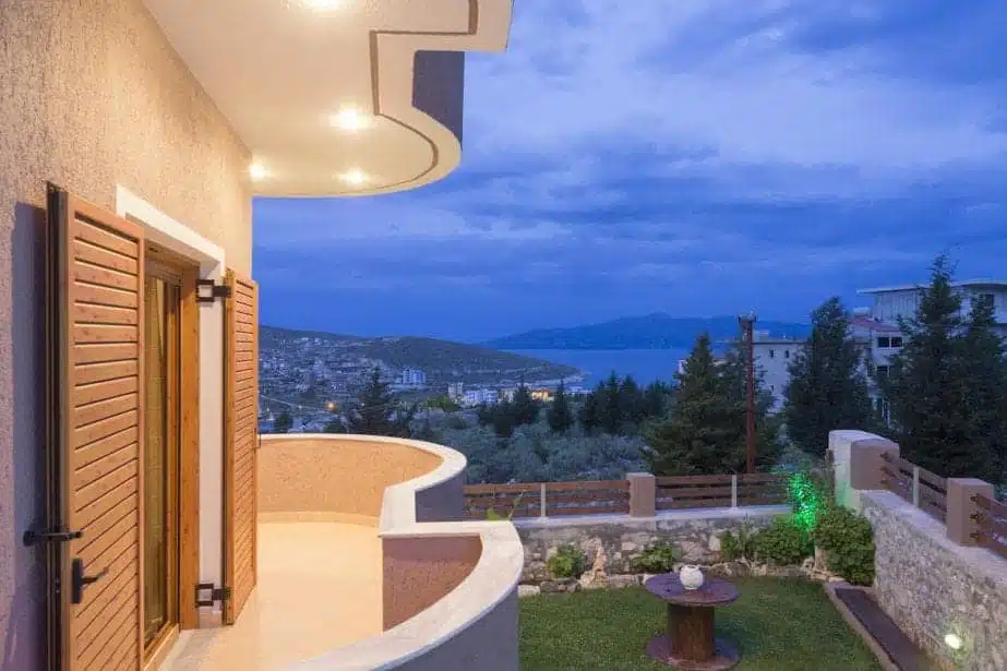 20 hoteles increíbles en Saranda, Albania Agradables hoteles familiares en Albania, balcón de la habitación del hotel con vistas a la zona del jardín cubierto de hierba y al otro lado de la bahía sobre una gran masa de agua hacia las montañas a lo lejos