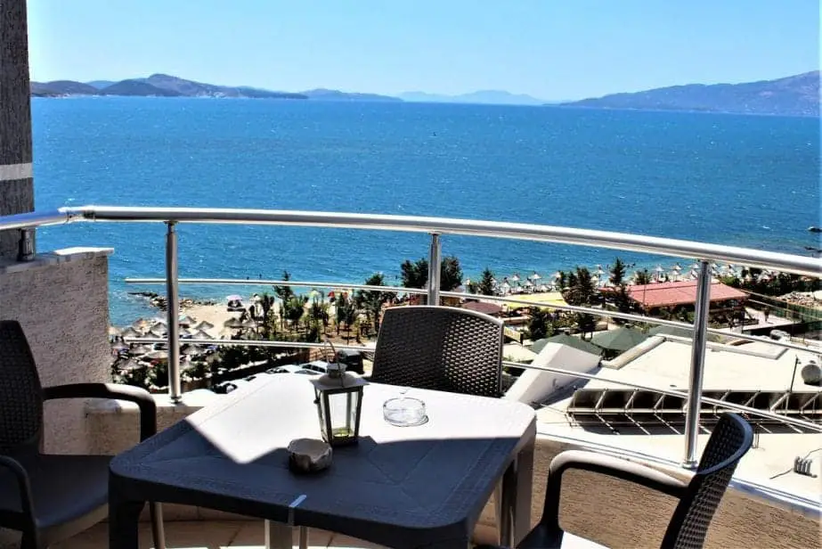 Visite el mejor resort en Albania, balcón con mesa y sillas con vista a los tejados hacia la playa con mar azul y montañas a lo lejos