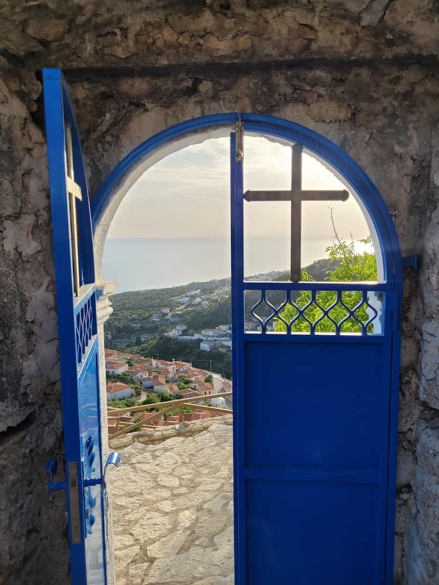 Puerta de metal azul con cruz que se abre hacia adentro con vista al pueblo de montaña afuera